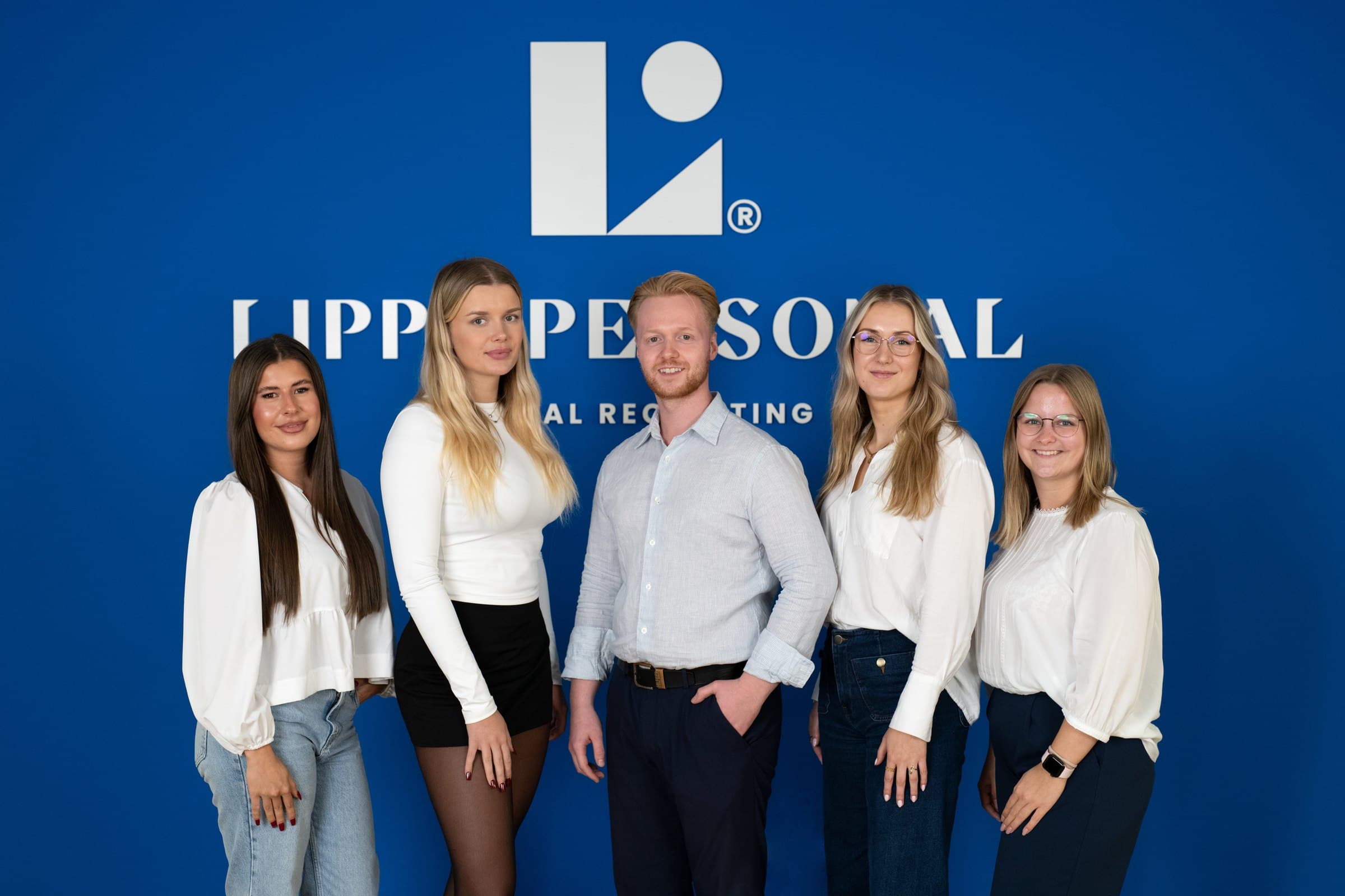 Junges Team von Lippe Personal vor der Logowand im Büro